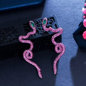 Gunmetal snake dangle earrings with purple zircon and green stone eyes on jewelry box
