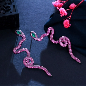 Detail of snake earrings with pink cubic zirconia stones and green gem eyes in black gold