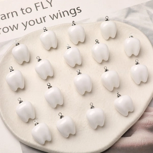Set of 18 cute white resin tooth charms with silver loops arranged in a heart tray