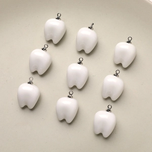 Top view of nine white resin tooth charms with silver metal rings for DIY jewelry making