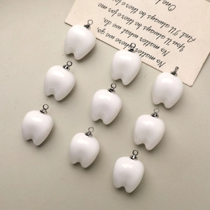 Detailed view of nine glossy white resin tooth charms with silver metal rings for DIY