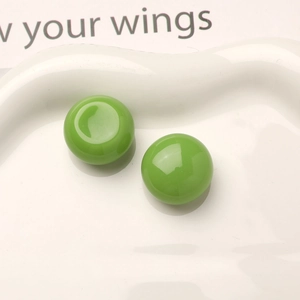 Macro shot of two glossy bright green resin cabochons on a white textured ceramic plate
