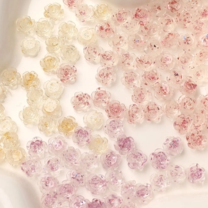Macro shot of transparent resin camellia flower nail charms with gold foil and glitter