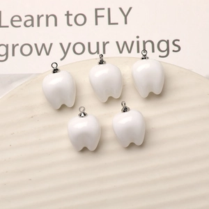Macro shot of five white glossy resin tooth charms with silver loops for DIY jewelry