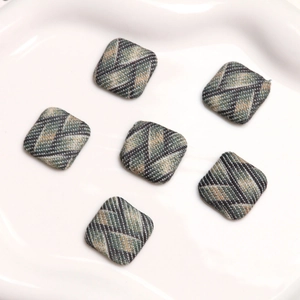 Macro view of six tweed plaid square fabric buttons on a white ceramic tray