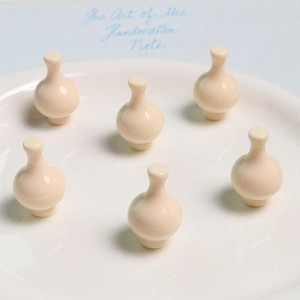 Dettaglio di sei ciondoli in resina bianco crema a forma di vaso su un vassoio bianco