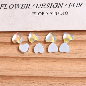 Macro shot of 8 aurora crystal and white heart-shaped nail art charms on wood
