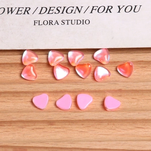 Close-up of heart-shaped iridescent and pastel pink nail art charms on a wooden display