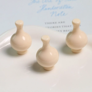 Dettaglio di tre ciondoli a forma di vaso in resina color crema su vassoio in ceramica