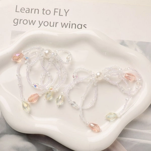 Detail view of handmade beaded bow earrings with pink crystal pendants on ceramic plate