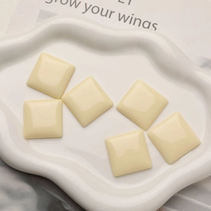 Close-up of six cream square resin charms for DIY jewelry making on a white tray