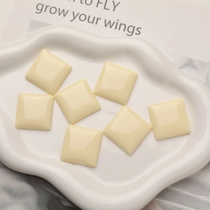 Close-up of square cream resin cabochons in a white ceramic dish for DIY jewelry making