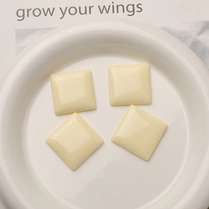 Detailed view of four cream square resin charms for DIY earrings on a ceramic plate