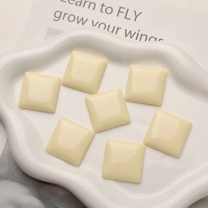 Flat lay of cream square resin cabochons on a white cloud-shaped ceramic tray for DIY craft