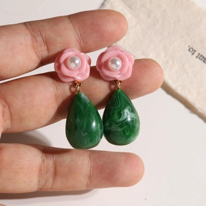 Close-up of DIY resin flower earrings with pearl centers and marble green drop charms