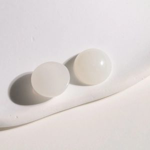 Vue macro de deux cabochons ronds en résine blanc laiteux sur un présentoir minimaliste