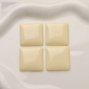 Macro view of four square cream resin flatback cabochons on a white wavy ceramic plate