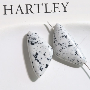 Close-up of white triangle turquoise beads with black ink splatter for DIY jewelry making