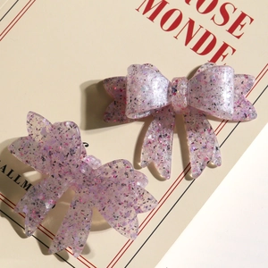 Detail view of glittery resin bow hair clips with purple and pink sequins on book prop