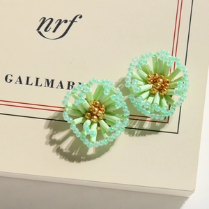 Close-up of handmade mint green and gold beaded floral earrings with a dandelion-like design