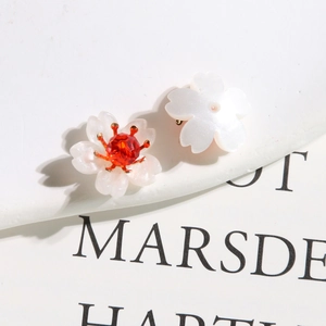 Detailed view of pearl white flower earrings with red crystal centers on a white background