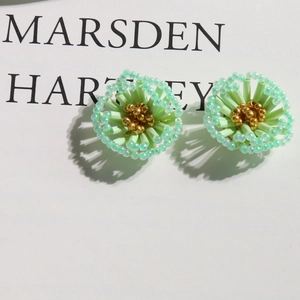Macro detail of hand-woven pastel green floral earrings with gold bead centers