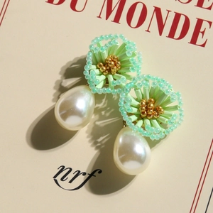 Detail of handmade green bead flower earrings with cream white teardrop pearls on a book