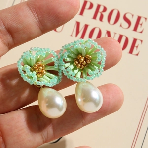 Detail of beaded floral earrings with drop pearl pendants held against beige card