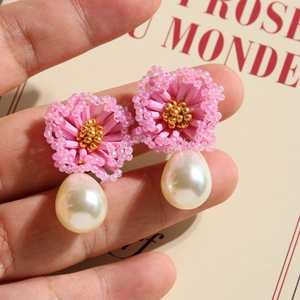Macro shot of pink bead flower earrings with white teardrop pearl drops on fingers