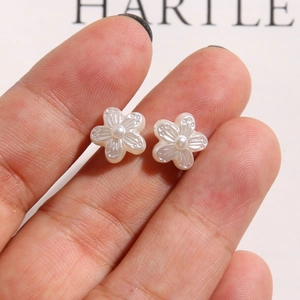 Close-up of small white camellia flower earring with a pearl center held in fingers
