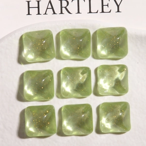 Close-up of nine square avocado green resin charms with gold glitter for DIY earring making