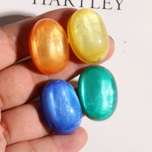 Close-up of four colorful oval glitter resin cabochons held in hand for DIY jewelry making