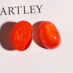 Macro detail of orange oval resin charms with gold glitter sand for DIY jewelry making
