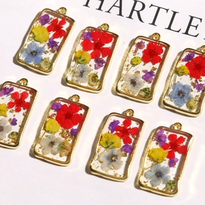 Macro view of rectangular alloy charms with real dried flowers and gold foil accents