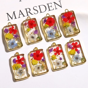 Detailed macro view of handmade rectangular resin pendants with dried flowers and gold foil
