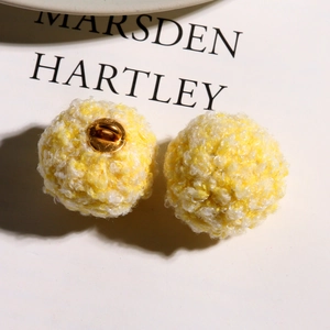 Detailed macro view of yellow and white plush fluffy balls with gold metal rings for DIY jewelry