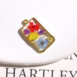 Macro view of rectangular resin pendant with colorful dried flowers and gold leaf