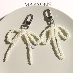 Elegant white pearl bow charm with silver lobster clasp on a minimalist display tray
