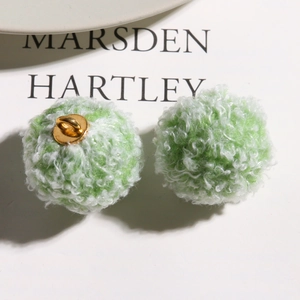 Macro shot of green and white curly faux fur pompom with a gold metal hanging loop