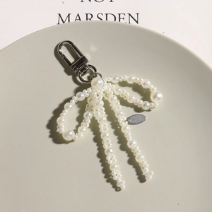 Elegant pearl bow pendant keychain with silver lobster clasp and tassel on a display tray