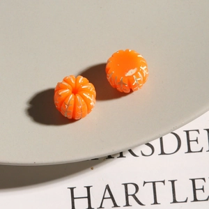 Makro-Detail von orangefarbenen Harzperlen in Kürbisform mit silberner Gravur für DIY-Schmuck