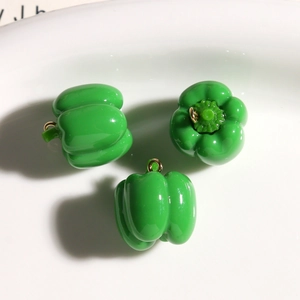 Three green resin bell pepper charms with gold hooks on white ceramic tray