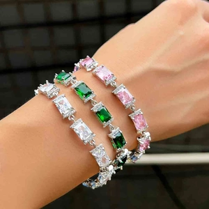 Dettaglio di bracciali in argento sovrapposti con zirconi rettangolari verdi, rosa e bianchi