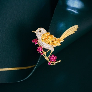 Macro detail of bird brooch with zircon stones and ruby flowers on gold branch