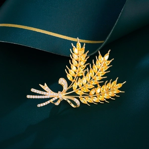Elegant gold wheat brooch with sparkling zircons and bow tie detail on a green surface