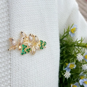 Elegant gold bird brooch with white zircon and green stones on white sweater