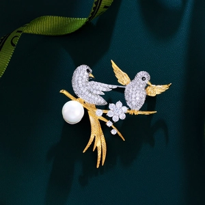 Macro detail of bird brooch with white zircon pavé, large pearl, and golden finish