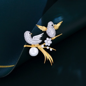 Detail of gold-plated bird brooch featuring white sparkling zircons and a large round pearl