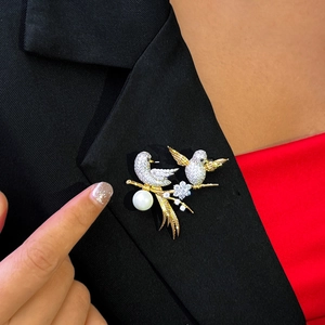 Elegant gold-plated twin birds brooch with white pearl and diamonds on a black suit lapel