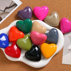 Close-up of vibrant heart charms in a white ceramic dish on a cork wood background